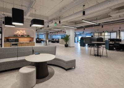VusionGroup office lounge with curved gray seating, open workstations, and a coffee station beneath an illuminated Dallas sign