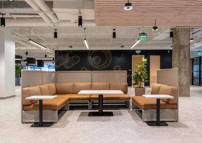 Collaboration area with tan sectional seating, tall privacy screens, and white tables beneath a wood slat ceiling