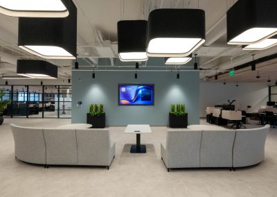 Curved gray sofas facing a wall-mounted screen on a blue accent wall beneath oversized black pendant lights