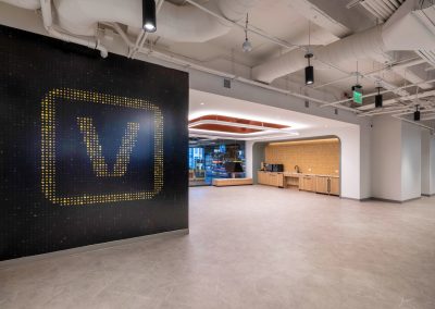 Large yellow Vusion logo on a dark feature wall beside a coffee bar and glass-enclosed retail showroom.